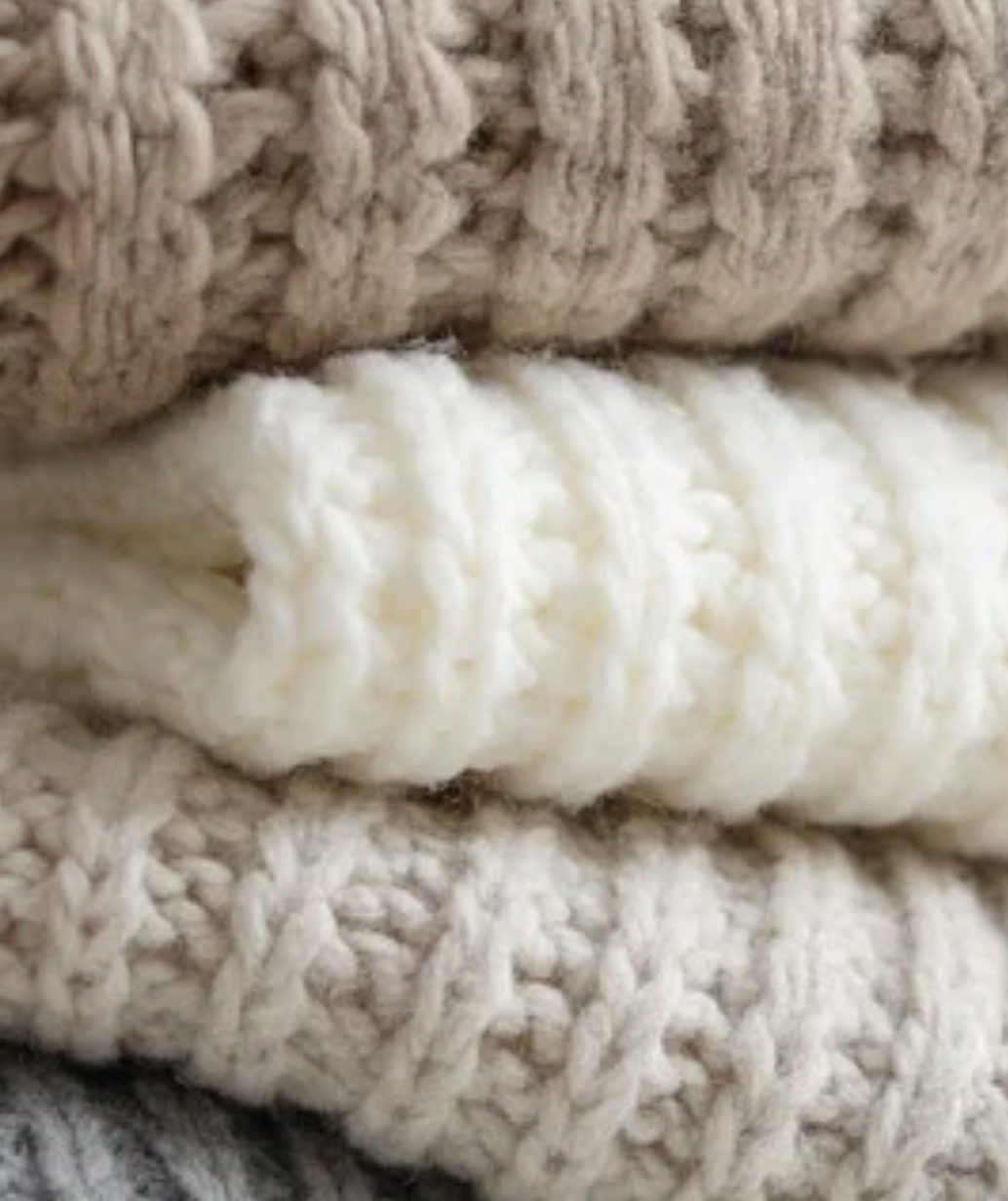 A stack of folded cashmere knits in cream and taupe