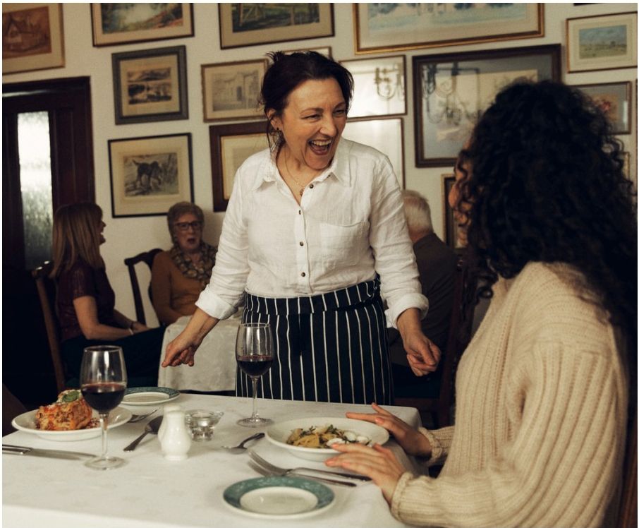 A laughing host serving food at a candlelit table